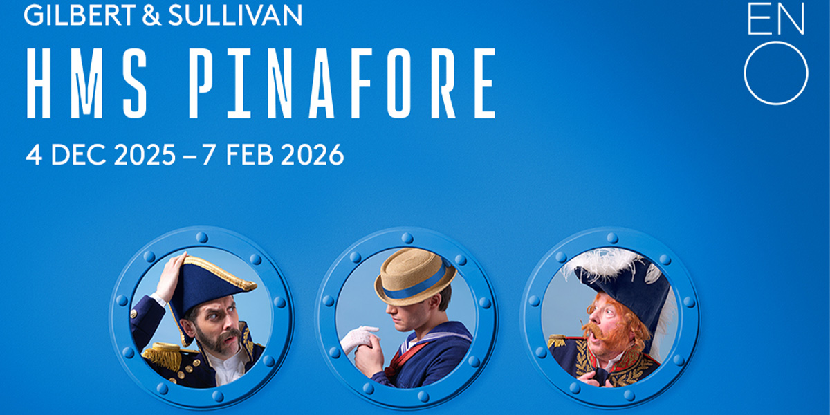 A woman in a blue and white striped pinafore stands on stage, smiling, with a theatrical backdrop.