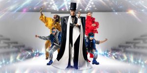 Four performers stand in dynamic poses, wearing stylish, colourful outfits against a sparkling light effect background.