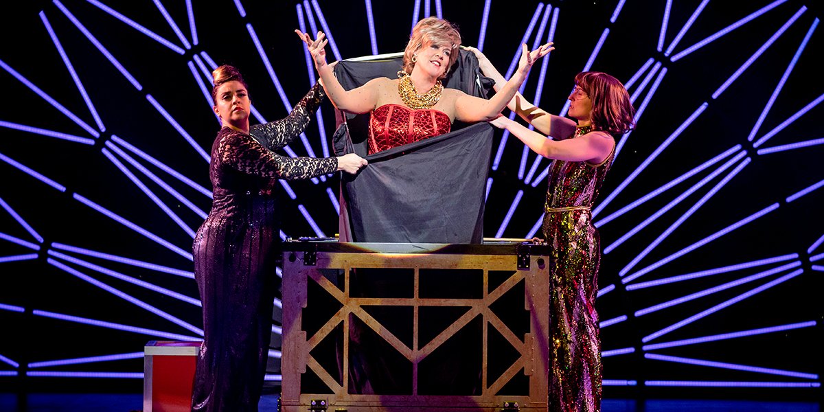 Three performers in vibrant costumes on stage during a magic act.