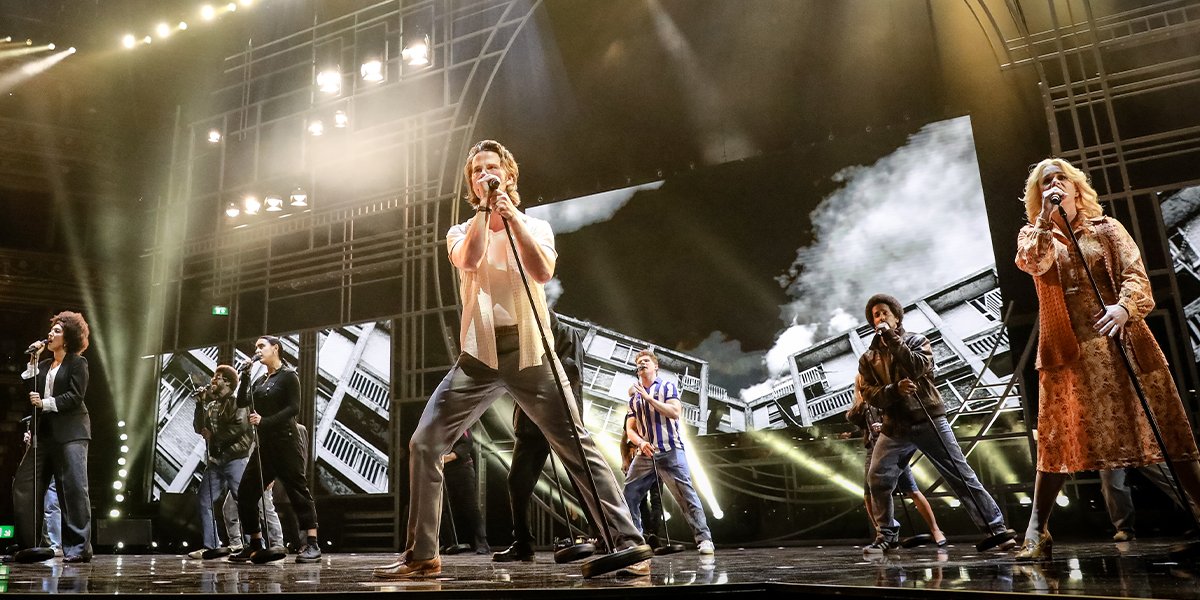 Olivier Awards 2023 highlights: a man in formal attire stands confidently, smiling against a vibrant backdrop.