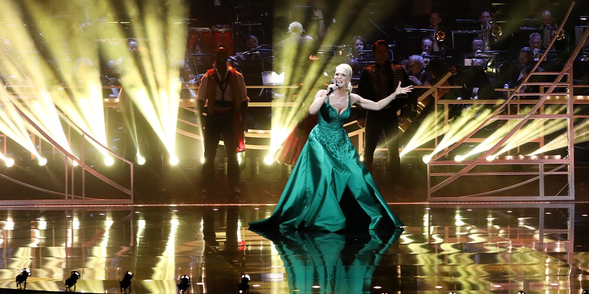 Hannah stands smiling among the Olivier Awards winners, wearing a black dress with gold accents.