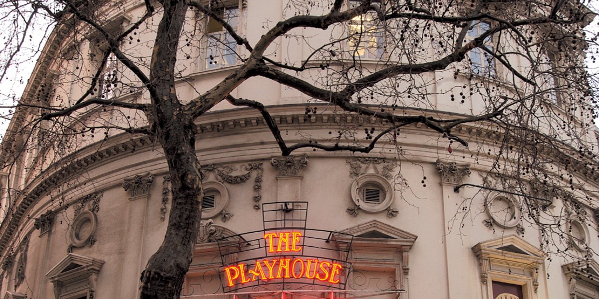 The Playhouse Theatre in London, featuring a red brick facade and a clear blue sky background.