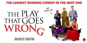 A chaotic scene with actors in formal attire, one falling, surrounded by scattered props and a dishevelled set.