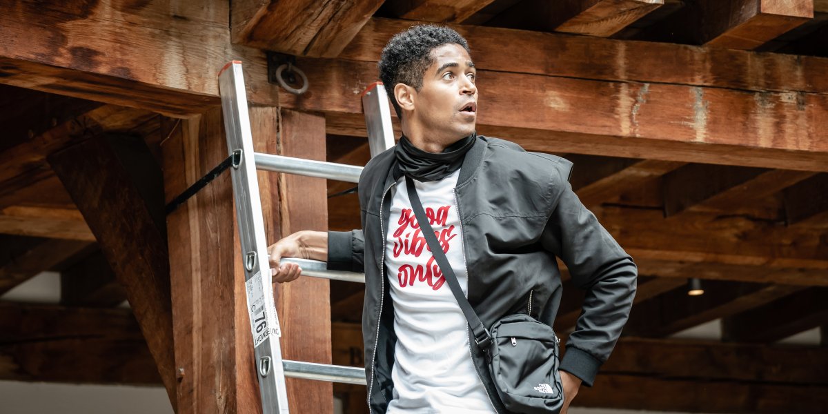 A young man in a black jacket and white shirt stands by a ladder, looking surprised.
