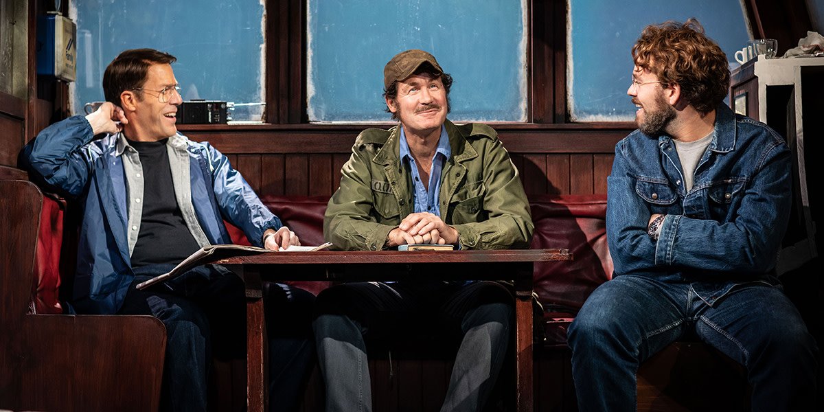 A promotional image for "The Shark Is Broken," featuring a large shark model against a blue background.