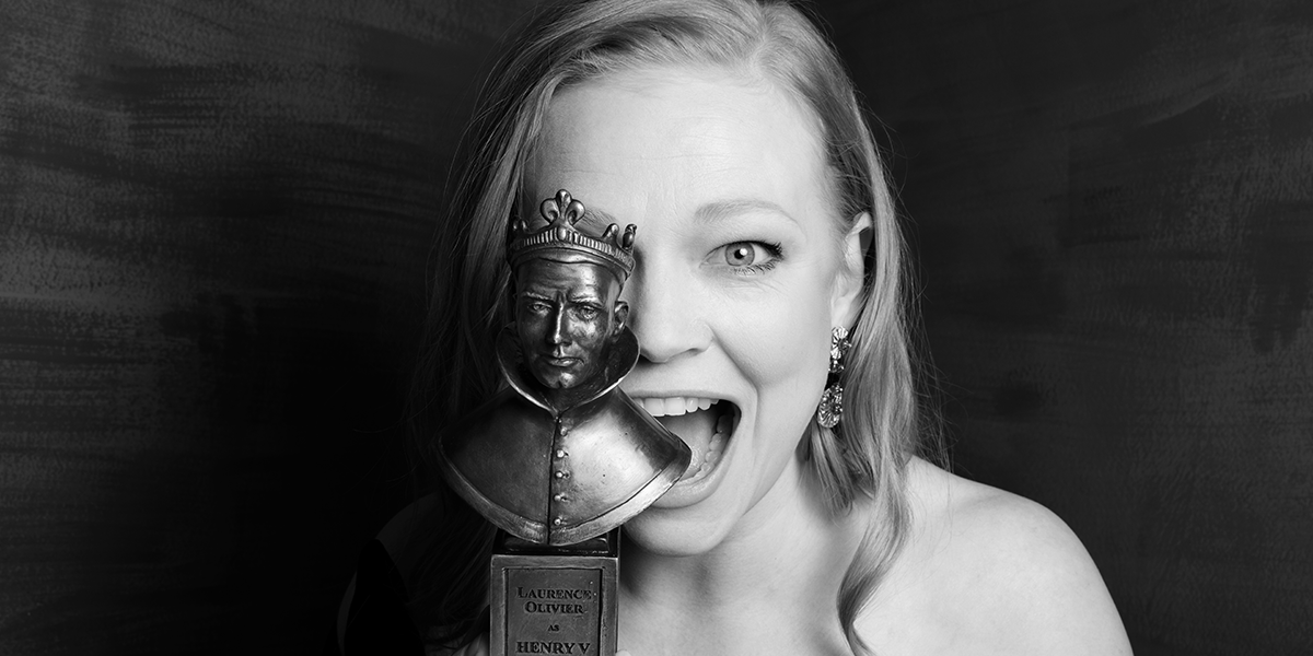 A black and white image of a person holding an award over half their face and smiling.
